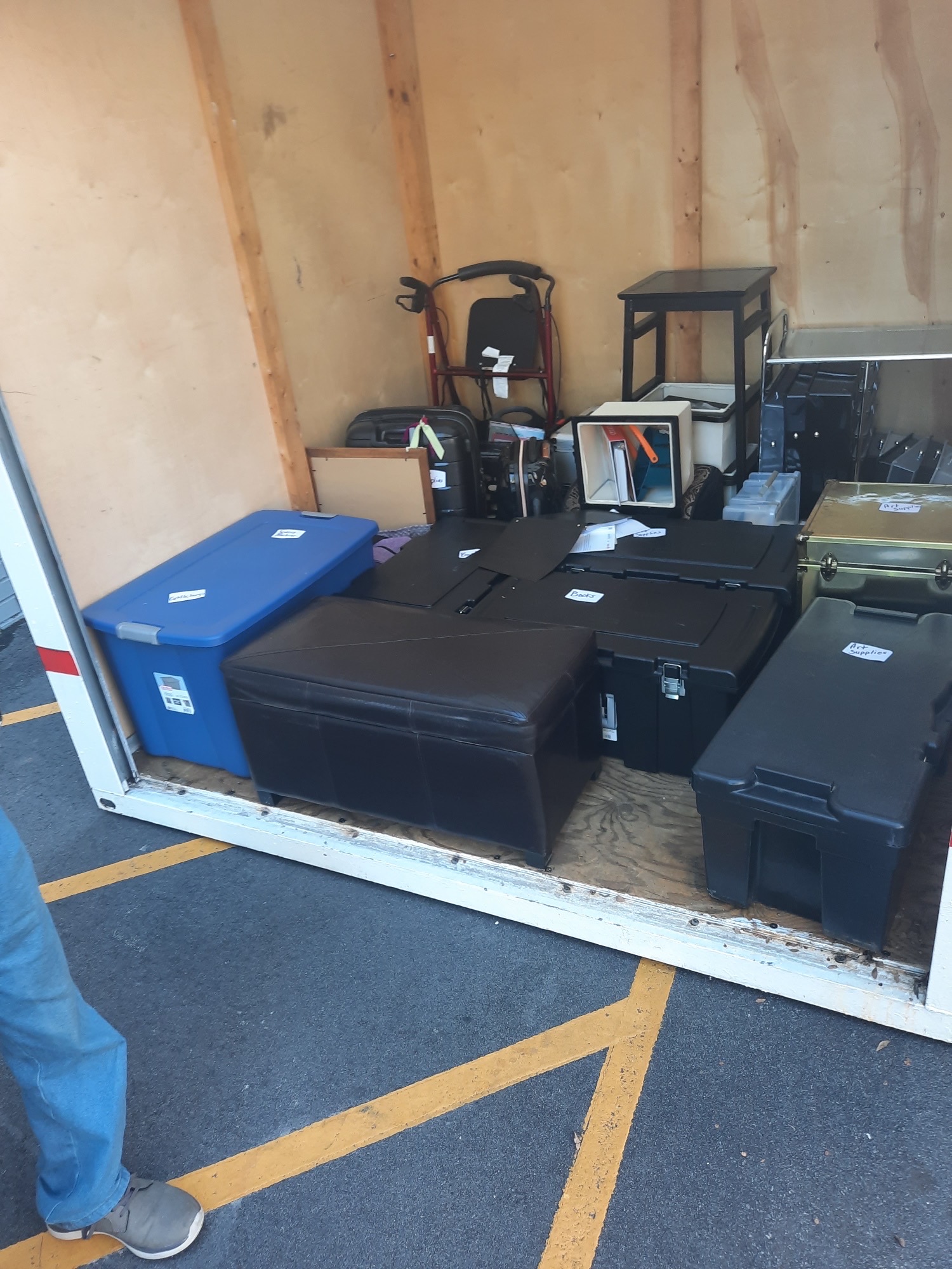 Enclosed trailer loaded with labeled storage totes, trunks and an ottoman ready for transport