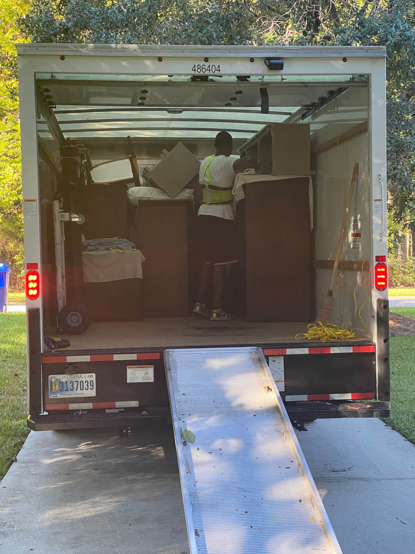 Mover loading wrapped furniture into a box truck with the ramp down in a driveway