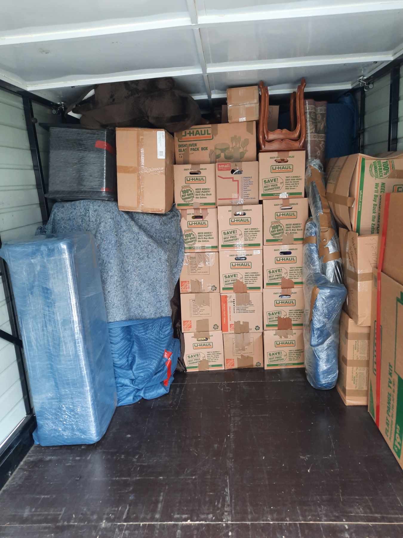 Moving truck packed wall to wall with stacked boxes, wrapped mattresses and blanketed furniture